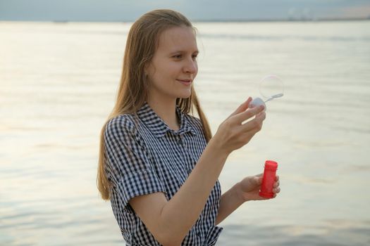 teenager blowing soup bubbles, beach on background, closeup, side view