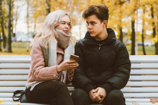 Young beautiful blonde girl blames her boyfriend by pointing finger to the phone screen. The concept of jealousy, quarrels, difficulties in communicating through social networks