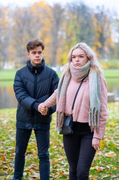 Two teenagers in love in a quarrel. The blonde girl takes offense at the boy, the guy holds her hand, asks the girl to stay and not leave. Concept of difficulties in adolescent relationships
