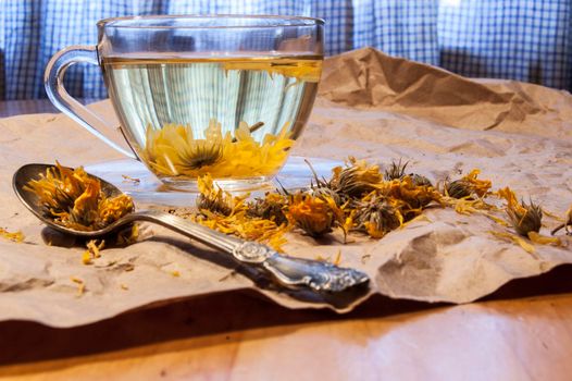 Glass cup of herbal tea. Near teaspoon dried marigold flowers and on the packaging paper.