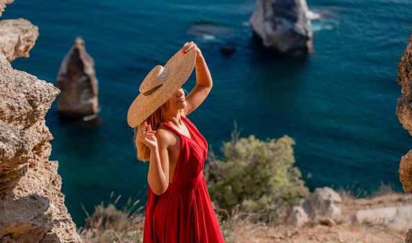 A woman in a flying red dress fluttering in the wind and a straw hat against the backdrop of the sea