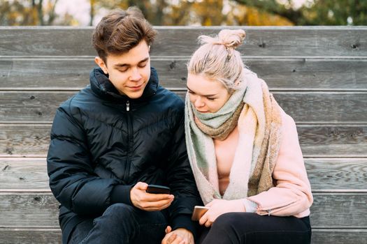 Loving teenagers on date look at mobile phones, guy shows the girl something interesting on the phone. Immersion in virtual world, social networks. Concept of teen love, Smombie dating