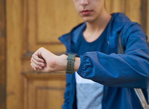 Young adult looks at the clock, waiting for a meeting with friends. A man is waiting for a woman in a street of city on a date, looking at the watch, copy space, close up