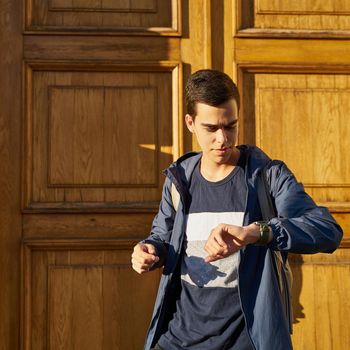 Young adult looks at watch. Stressed caucasian man with black hair afraid of getting late. Girlfriend is late for a date