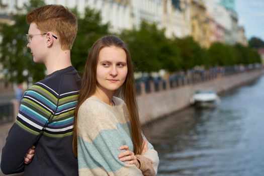 portrait of a happy couple, standing back to back in the city center, red-haired man in glasses, beautiful woman with long dark hair, copy space