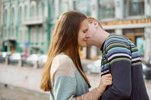 portrait of happy couple embracing in downtown, red-haired man with glasses kisses or whispers woman with long hair, copy space