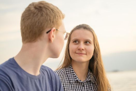 female and male person looking at each other, concept of love on the beach, sea background, closeup side view