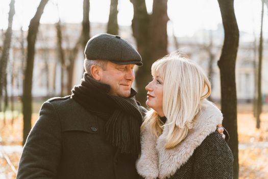 Closeup portrait of a happy blonde mature woman and a beautiful brunette middle-aged man looking at each other's eyes. Loving couple 45-50 years old walks in the autumn park in warm clothes