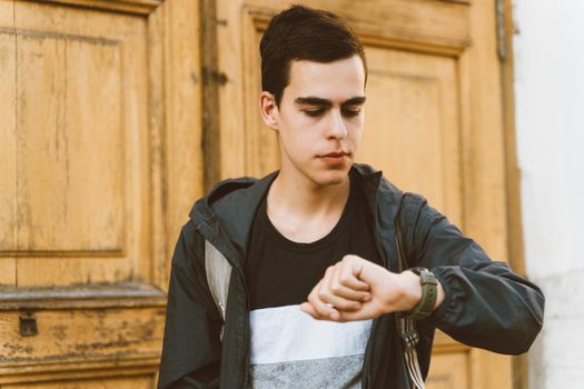 Young adult guy looks at watch. lost time, the concept of lack of time. Stressed caucasian man with black hair afraid of getting late. Girl is late for a date