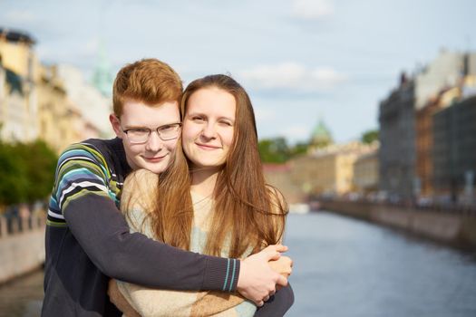 portrait of happy couple embracing in downtown, red-haired man with glasses, woman with long hair looking straight, copy space