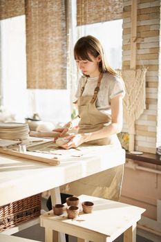 Beautiful young woman making ceramic ware, roll out with a rolling pin in sun light. Concept for woman in freelance, business, hobby