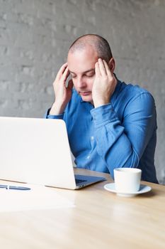 A man suffers a headache, sits at work in the office at a laptop, rubs his hands with whiskey. The concept of overwork, stress, processing, vertical