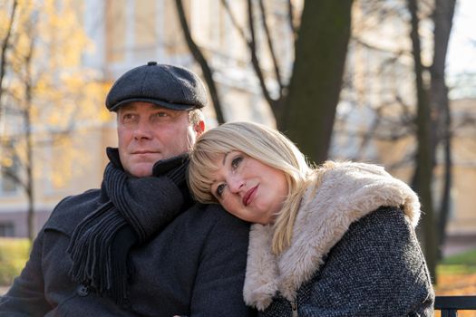 Closeup portrait of happy blonde mature woman and beautiful middle-aged brunette, looking away. Loving couple of 45-50 years old walks in the autumn park in warm clothes, in coat and enjoys life