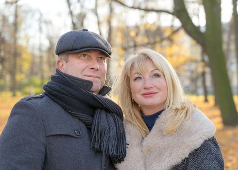 Closeup portrait of happy blonde mature woman and beautiful middle-aged brunette, look up to the sky. Loving couple of 45-50 years old walks in autumn park in warm clothes