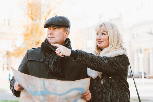 Happy blonde mature woman and handsome middle-aged brunette man travel and enjoy life. A loving couple is looking in a guidebook and looking for sights, standing in the center of a European city.