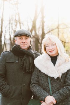 Closeup portrait of happy blonde mature woman and beautiful middle-aged brunette, looking looking directly at camera. Loving couple of 45-50 years old walks in autumn park in warm clothes, vertical