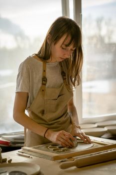 Beautiful young woman making ceramic ware, molding a shape in workplace in sun light. Concept for woman in freelance, business, hobby