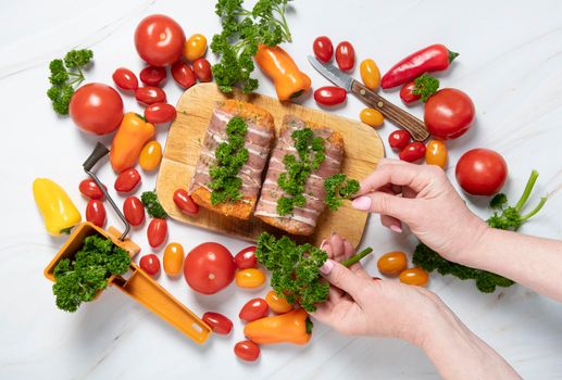 female hands decorate with parsley minced meat sausages in bacon with fresh vegetables, cherry tomatoes, sweet peppers, colorful food flat lay. High quality photo