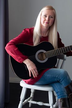 beautiful young blonde woman in a red dress with a black guitar, favorite hobby, music project. High quality photo