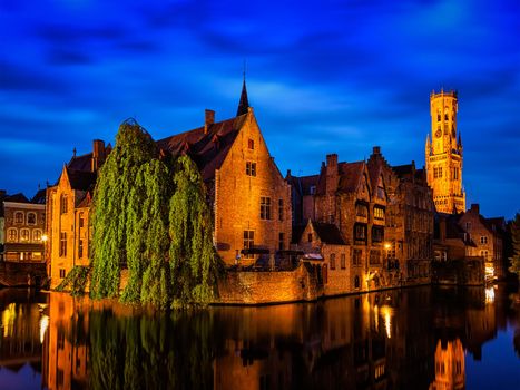 Famous view of Bruges - Rozenhoedkaai with Belfry and old houses along canal with tree in the night. Brugge, Belgium