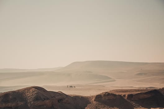 Endless yellow sandy hot desert. Lonely Egyptians on camels are walking in the distance.