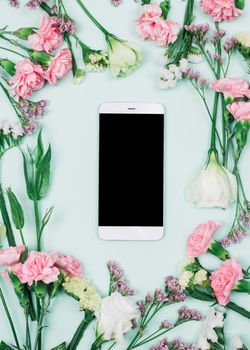 blank smartphone surrounded with fresh limonium carnations eustoma flowers against blue background