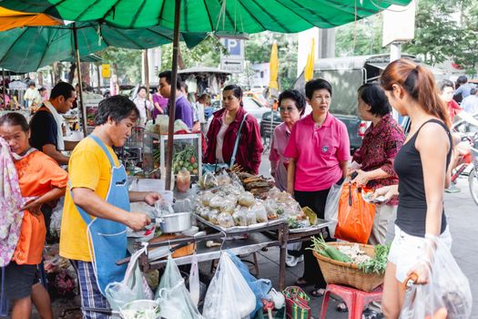 BANGKOK, THAILAND - October 23, 2012. Local people and tourists buy food on street market. Fruits and ready-to-eat soups and sauces in plastic bags.