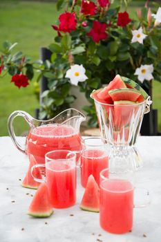 a woman in a green dress pours a red refreshing drink from the pulp of a watermelon into a glass glass, bright natural background