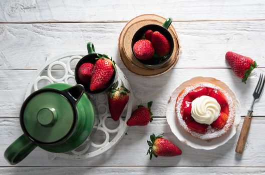 Fruit still life with strawberries and green tea set, strawberry cake with cream sweet dessert, female hand breaks off a piece of cake with a dessert fork. High quality photo