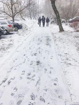 Three men walk down the street covered with snow. Footprints on snowy pavement. Winter in town.