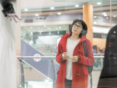 Woman stares on dummies in clothing store. Casual outfit hanging on mannequins. View through transparent shop window. Shopping at mall. Basic clothes for everyday wear. Modern urban fashion.