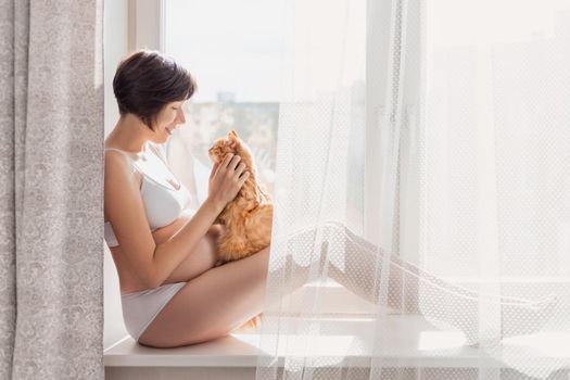 Pregnant woman in white underwear with cute ginger cat. Woman in lingerie expecting baby. Risk of infection toxoplasmosis.