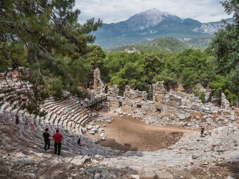PHASELIS, TURKEY - May 19, 2018. Tourists walk into ruins of amphitheatre of ancient Phaselis city. Panorama view on famous architectural landmark, Kemer district, Antalya province.