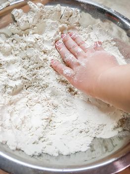 Little child is touching flour in metal bowl. Cooking with children. Developing fine motor skills by letting to touch food ingredients.