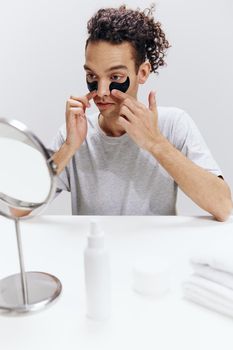 handsome guy in a white T-shirt sits at a table with a mirror and a towel face patches skin care. High quality photo