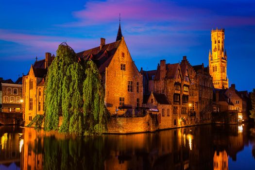 Famous view of Bruges - Rozenhoedkaai with Belfry and old houses along canal with tree in the night. Brugge, Belgium