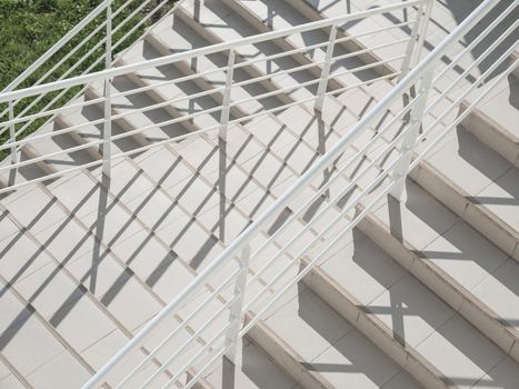 White exterior of outdoor staircase with railing. Sunlight and shadow on stone steps. Urban geometry.