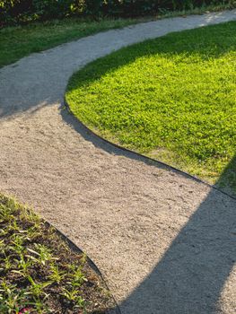 Walking path winding among lawns in garden. Landscaping in park.