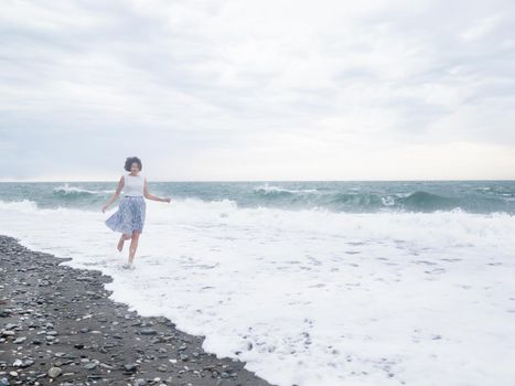 Happy woman is running on surf of stormy sea. Woman with hair ruffled with the wind. Wanderlust concept. Vacation on sea coast.