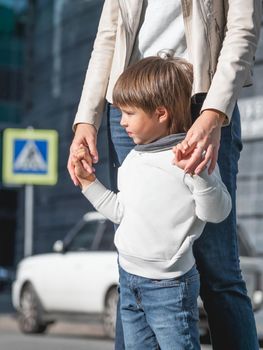 Mother and son stand on street in sunlight. Woman and kid in modern town with transport traffic and road sign. Family in city.