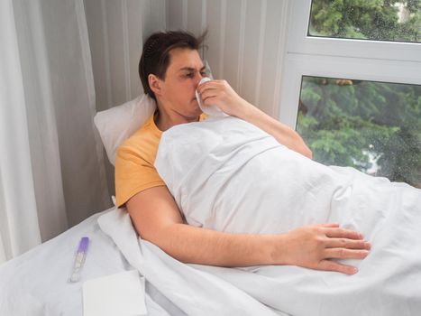 Sick man is lying in bed with thermometer. Man is blowing his nose. Temporary disability in case of disease symptoms.