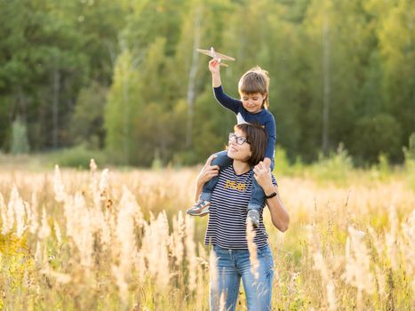 Cute boy and his mother play with toy air plane. Happy kid dreams to be a pilot. Boy is planning for the future. Mom and son on field at golden sunset hour at autumn season.