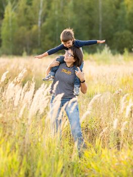 Cute boy and his mother play as airplane. Happy kid dreams to be a pilot. Boy is planning for the future. Mom and son on field at golden sunset hour at autumn season.