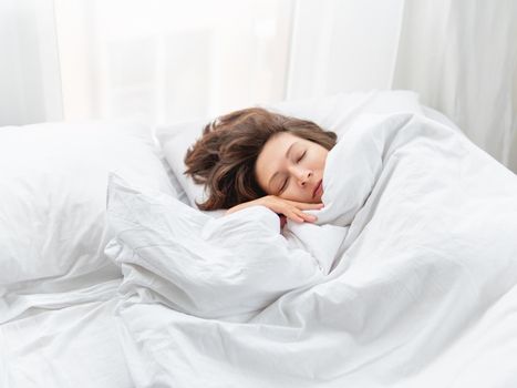 Caucasian woman is sleeping in bed. Healthy sleep on white bed linen. Morning at cozy home.