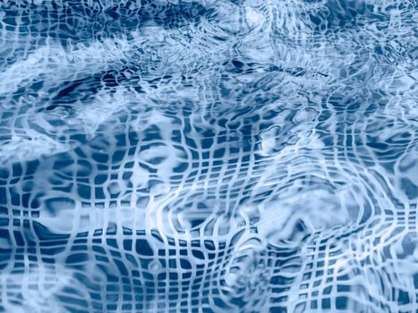 Surface of water in swimming pool or fountain with blue mosaic bottom. Abstract background with wavy pattern of clear transparent water.