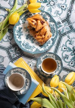 flat lay food, sweet puff, tea in a vintage porcelain cup and a stack of books, a bouquet of yellow withering tulips in a vase,. High quality photo