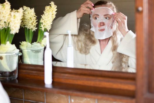 a middle-aged woman is busy with morning hygiene, trying in vain to straighten the mask with cleansing and moisturizing impregnation on her face High quality photo