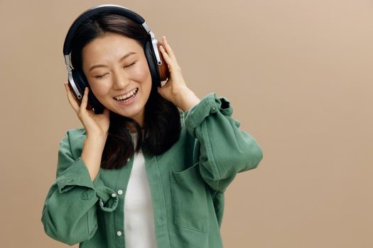 Relaxing enjoyed fav song cute Asian student young woman in khaki green shirt touch headphones posing isolated on over beige pastel studio background. Cool fashion offer. Music App Platform Ad concept