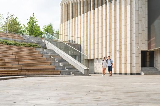 Adult students walk near outdoor audience with wooden seats near university campus. Young couple on romantic date. Summer vibes. Education in Europe.