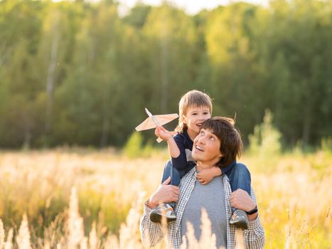 Cute boy and his father play with toy air plane. Happy kid dreams to be a pilot. Boy is planning for the future. Dad and son on field at golden sunset hour at autumn season.